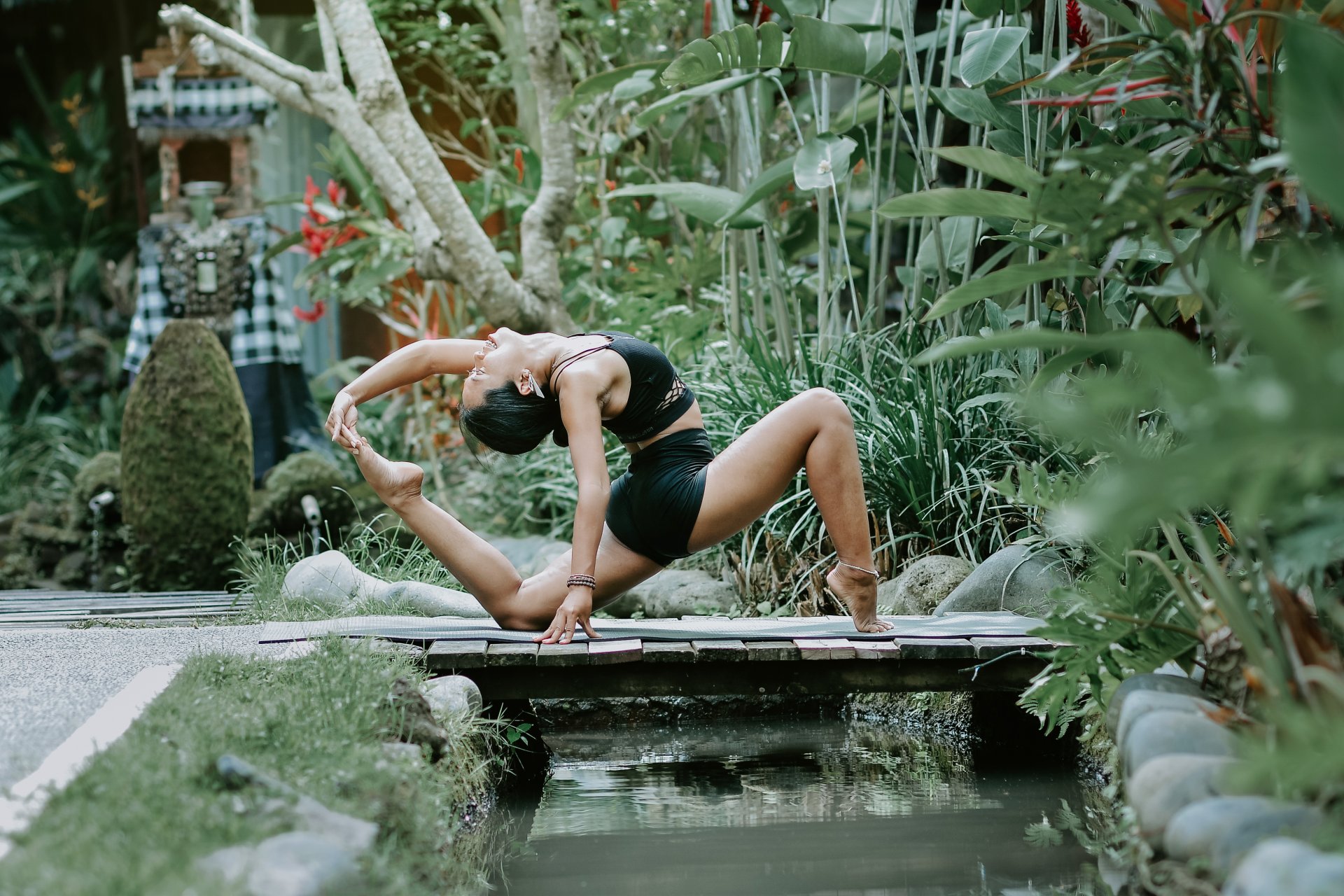 Oka Pastini in a deep backbend on a mat over a garden pond at her yoga space in Bali